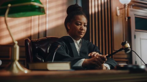 Court of Law Trial in Session: Portrait of Honorable Female Judge Reading Decision, striking Gavel. Presiding Justice Pronouncing Judgment Sentence. Innocent or Guilty Verdict. Cinematic Dramatic Shot