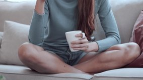 Video of pretty young smiling woman listening music with mobile phone while drinking cup of coffee sitting on a couch at home.