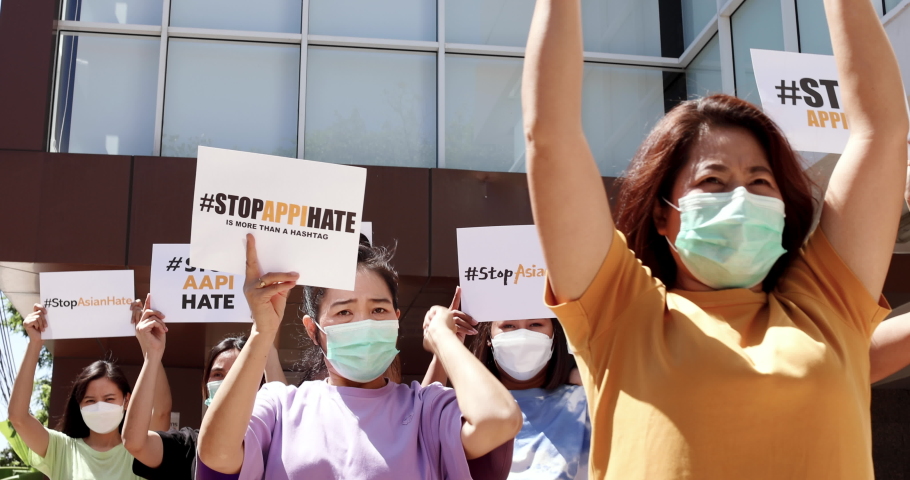 Asian women wearing protective hygiene face masks show banners and rise punches during participants in Asian American Pacific Islanders rally marching protest to stop hate on AAPI citizens. Royalty-Free Stock Footage #1078118384