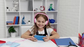 happy amazed teen girl in headphones watching video on smartphone in classroom, online education