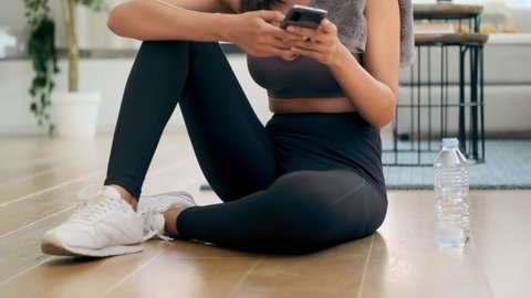Video of sporty young woman using her mobile phone while listening to music after a pilates class on the floor at home.