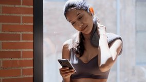 Video of sporty young woman sending messages with her smart phone while take a break of exercise in living room at home.