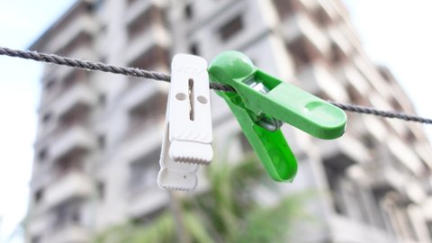 White and green two cloth fastening clips are hanging on a plastic rope. Clothespins on the rope. Plastic clothespins on a rope in the high res building and sky background. 4k video.