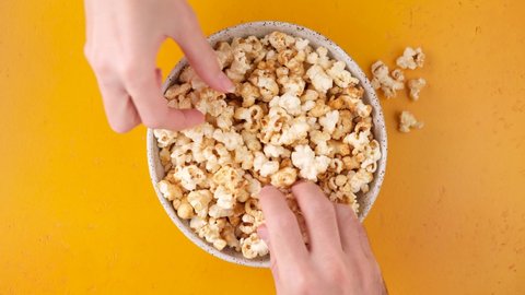 Young male and female hands grab popcorn. Bowl of salty and sweet popcorn on yellow background. Top view