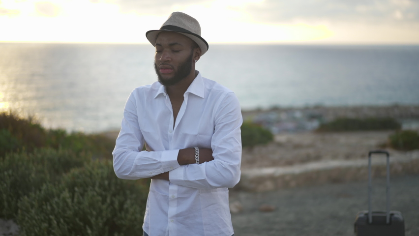 Sad African American gay man standing on Mediterranean sea coast at sunset with crossed hands procrastinating. Portrait of hopeless depressed handsome LGBT person outdoors thinking. Inequality concept Royalty-Free Stock Footage #1078126871