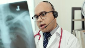 Doctor talks to patient via online video conferencing with computer wearing headset. Explain about taking medications to treat illnesses holding x-ray film.