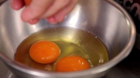 Slow motion of chef cracking egg into stainless bowl reveal egg yolk. To be made into a meal in kitchen. Cooking at home and homemade meal concept.