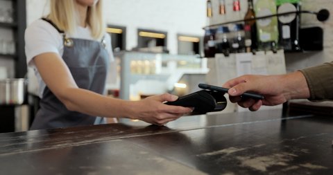 Close up male customer pays with contactless Nfc payment technology on smartphone to friendly barista in customer uses mobile to pay through bank terminal. Nfc cellhone of male buyer with cashless