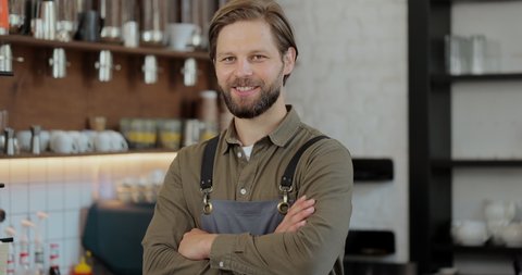 Successful small business owner man standing with crossed arms. Portrait of young male cafe owner. Coffee shop concept.
