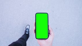 Man Walking and Use Green Screen Chroma Key Phone Point of View. Caucasian Person Hold in Hand Smartphone Mock-up and Watching Video Content, Browsing Internet News. Go in Urban Mobile Phone Close-up