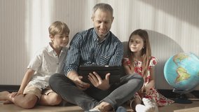 Family watching funny video by digital tablet and smiling. Father with children, boy and girl using portable device at home. Son, daughter and dad laughing, enjoying time together at home.