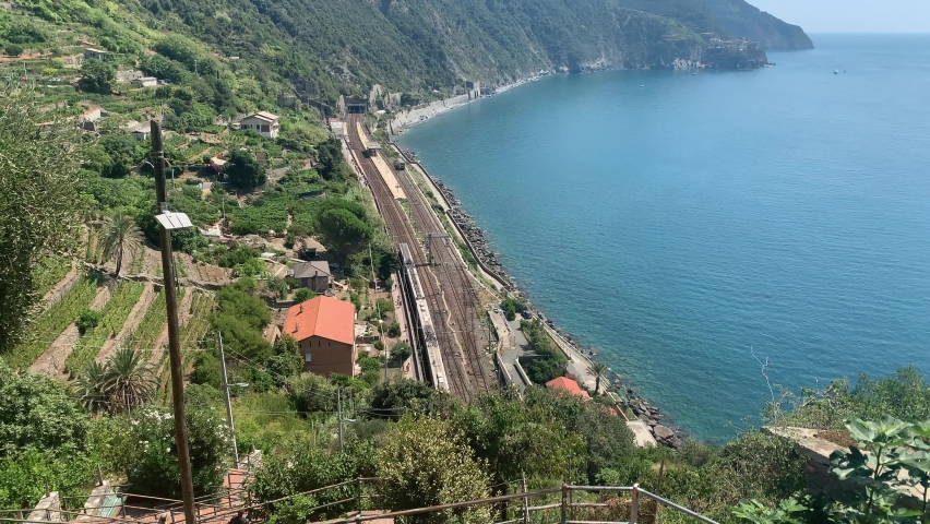 Italian Trenitalia train arrives at Corniglia (Cinque Terre) train, railway station in mountains. Italian riviera Mediterranean sea coastline.  Corniglia, Cinque Terre, Liguria, Italy. Royalty-Free Stock Footage #1078149491
