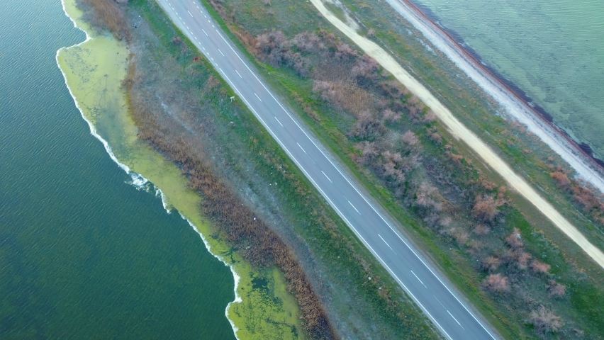 Aerial view of a red truck driving along a dam highway surrounded by lakes at sunset. Road between two lakes on a summer day.