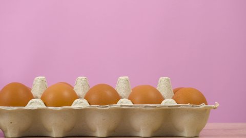 Open egg box with ten brown eggs on pink background. Many fresh raw chicken eggs in cartons, dolly. Chicken brown fresh raw eggs in an egg container.