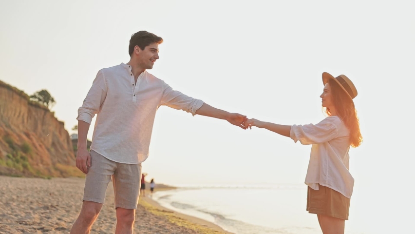 Smiling fun happy romantic young couple two friends family man woman 20s in white clothes dance hug look far away together at sunrise over sea beach ocean outdoor seaside in summer day sunset evening