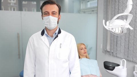 Smiling male professional dentist doctor man put off sterile face mask ppe look camera young woman patient on the background in dental clinic light office medical center with modern tools equipment