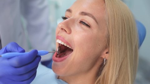 Satisfied young woman patient open mouth for examining with mouth mirror fixing whitening teeth in dental clinic light office medical center with modern tools equipment. Healthy lifestyle concept
