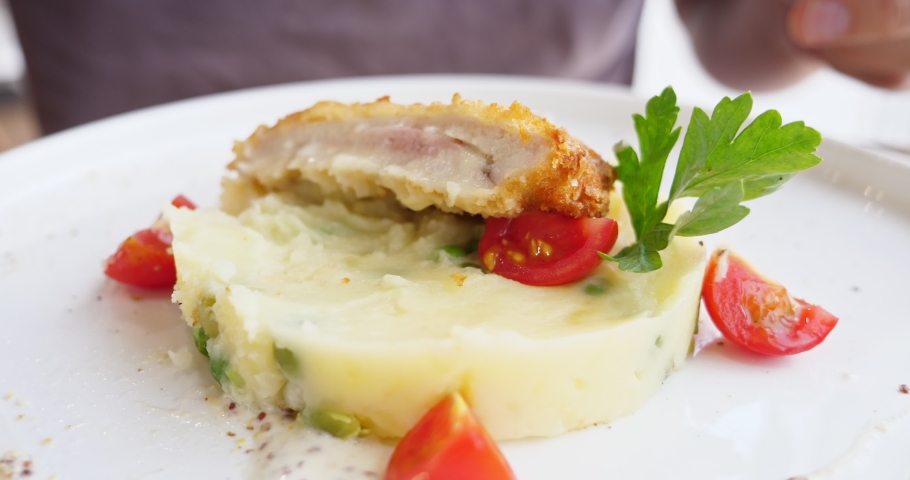 Close-up. someone eats with a knife and a fork cordon bleu with potato  cream and cherry tomatoes.
