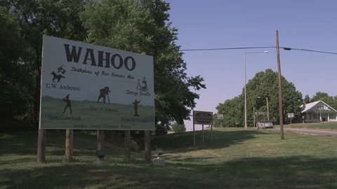 Static shot of the WAHOO, Nebraska sign as a car drives by in the background.