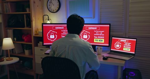 rear view of asian worried young man looking at computer with ransomware attack words on the screen in the evening at home