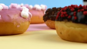 Close-up slider motion donuts. 4k closeup of delicious sweet multicolored donuts on colorful background. Confectionery baking, desserts.