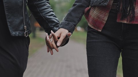 Close up shot with tracking of young female couple holding hands and walking in park on date