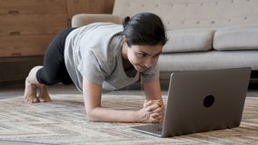 Young attractive woman doing sports at home and watching a video fitness lesson on a laptop