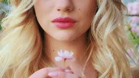 Closeup portrait of lower part face. Fresh healthy tender beautiful pink lips. Natural makeup cheekbones. Blond woman with long loose wavy hair. Girl holding lonely blooming sakura flower in hand