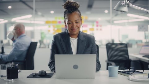 Portrait of a Happy African American Businesswoman Using Laptop Computer in Modern Office. Stylish Beautiful Manager Smiling, Working on Financial and Marketing Projects. Camera Zoom In.