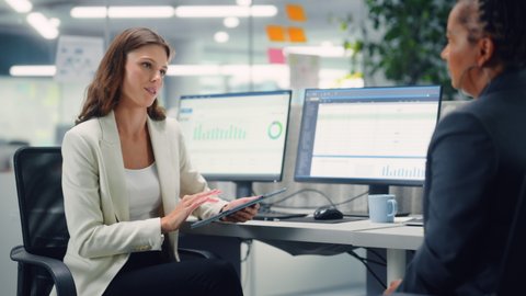 Two Female Colleagues Fondly Talk to Each Other, Smile while Showing Work on Laptop in Diverse Modern Business Office. Experienced Manager and Young Employee Discuss a Fun Analytical Project.