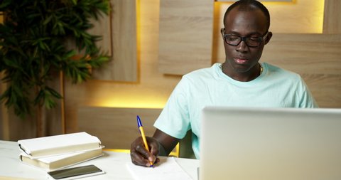 Handsome Black Student Studying Using Laptop, Writing a Lecture in Notebook. Close-up Face Portrait Focused African-American Man at Online Learning Process. Education Modern Technology. 
