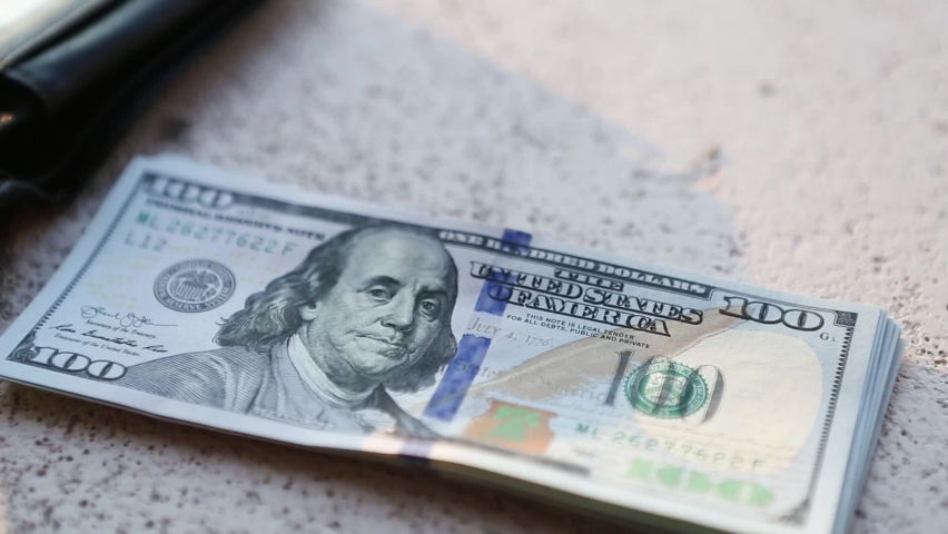 Hand puts a hundred-dollar bill in a pile and takes a banknote. Cash money, Stack of $100 bills in close-up. Finance, economy, financial planning, economics, savings.