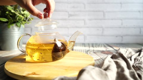 Female hand putting a wetted tea bag into glass teapot and adding hot water or pouring boiled water, cover teapot and steep tea to the correct amount of time. Brewing or making tea process video.