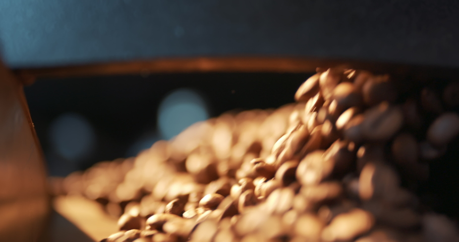 Roasted coffee beans fly and spin on a black background in slow motion. Production of fresh fried coffee beans roasting factory process. Prepared coffee beans mixing around on a cooling plate of oven. Royalty-Free Stock Footage #1078207265