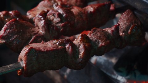 closeup of prepare and turning roasted shashlik meat on skewer on barbecue grill