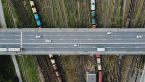 Aerial video from above of bridge with moving cars. There are many railway tracks under the bridge. Trains with cargo wagons and tanks drive along them. Import and export logistics. Freight terminal.