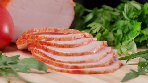 Slicing traditional ham into pieces on a wooden cutting board with a knife. Thin slices of meat. Concept of delicious food snacks and cooking.