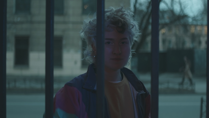 Young girl in retro bomber jacket opening courtyard gates, walking towards the camera and dancing vogue in evening