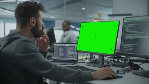 Multi-Ethnic Office: White IT Programmer Working on Computer with Green Screen Chroma Key Display. Male Software Engineer Developing App, Program, Video Game. Terminal with Code Language. Static Shot