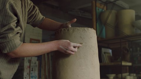 Woman potter is working in studio, scraping a big clay vase, modelling vessel's side, working skillfully by her hands, pottery art, Foreground, Slow motion.