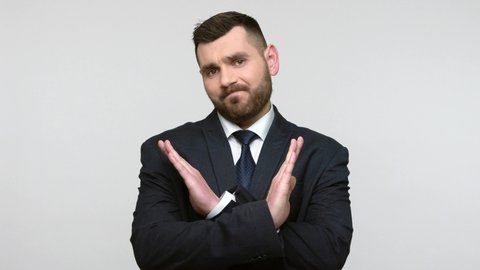 Bearded businessman in black official style suit crossing arms in X sign, refusal stop gesture, warning of prohibited access, declining communication. Indoor studio shot isolated on gray background.