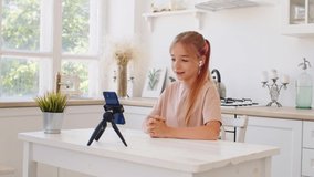 Teen girl having a video call via smartphone at home in kitchen