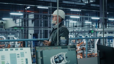 Car Factory Office: Portrait of Male Engineer Wearing Hard Hat Walking, Monitoring Production Conveyor with Tablet Computer. Automated Robot Arm Assembly Line Manufacturing High-Tech Electric Vehicles