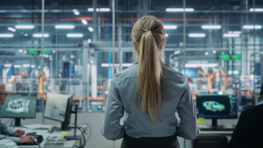 Car Factory Office: Successful Female Chief Engineer Overlooking Automated Robot Arm Assembly Line Manufacturing Advanced High-Tech Electric Vehicles. Production Conveyor. Back View Shot Royalty-Free Stock Footage #1078238009