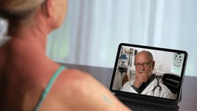 Senior male doctor videoconferencing woman remote patient consulting pandemic during telemedicine video call in conference virtual webcam chat app. Over shoulder laptop screen view