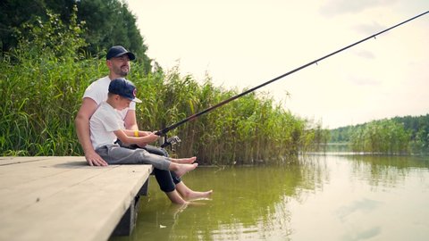 father with little children son catches fish standing on a wooden bridge or pier. Family dad and kids spend leisure time together camping teach fishing. Day vacation on lake or river outdoors
