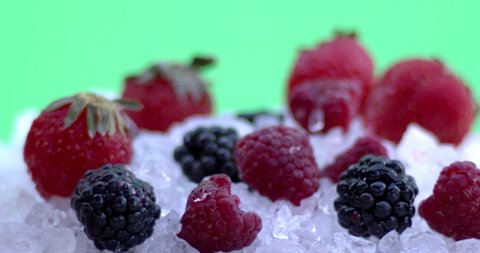 A drop of water falls on fresh and cold raspberries and blackberry in ice on a green background, natural berry for fresh juice, juice, cold tea or yogurt. Shooting close-up, slow motion. 4K.