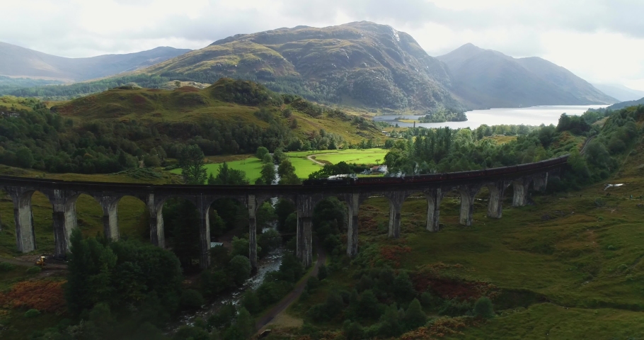 Aerial Drone View of the Hogwart's Express (Harry Potter) also known as the Jacobite Steam Train Crossing the Glenfinnan Viaduct with Loch Shiel in the Background in the Scottish Highlands, UK