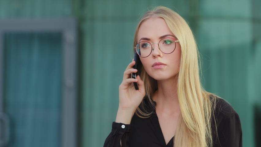 Worried nervous Caucasian European blonde woman holding mobile phone angrily talking to bank service outdoors. Customer dissatisfied with poor serve, annoyed client, aggressive businesswoman concept Royalty-Free Stock Footage #1078268873