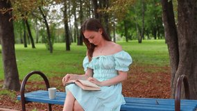 Beautiful girl reads a book on a bright summer day, sitting on a park bench. Girl enthusiastically reads a book and drinks tea outdoors